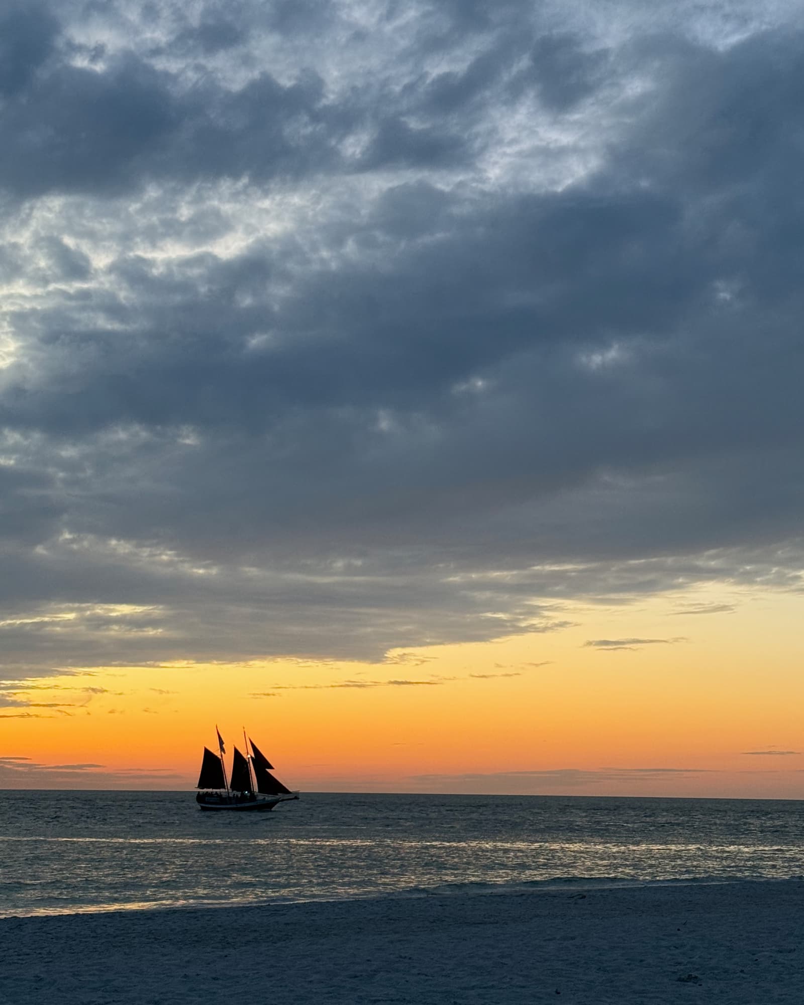 Sailboat on the ocean at sunset under dramatic clouds
